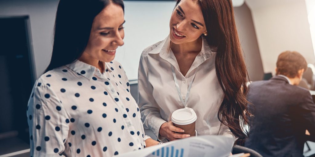 Two beautiful Caucasian female spending coffee time and looking through document from financial department